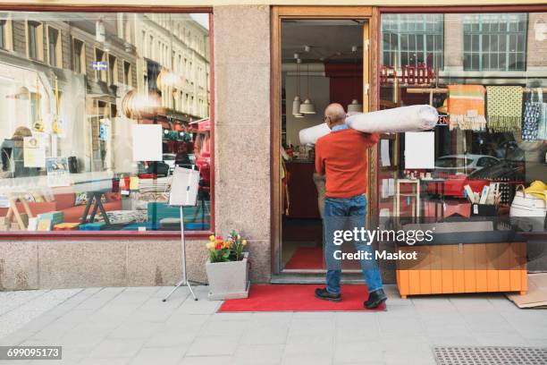 rear view of owner carrying rolled up carpet while walking towards store - carpet roll fotografías e imágenes de stock