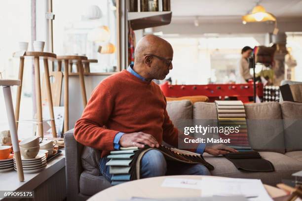 senior owner arranging fabric swatches while sitting on sofa at store - furniture store stockfoto's en -beelden