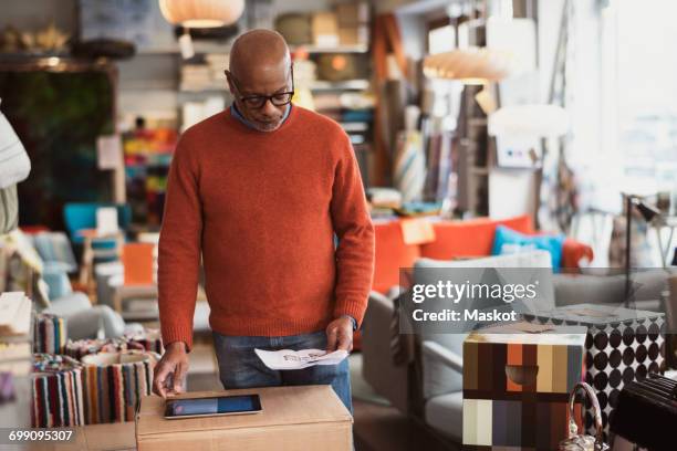 senior man using digital tablet while reading document at store - paper furniture stockfoto's en -beelden