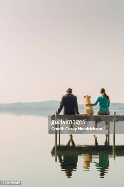 woman, dog and man relaxing on the end of long lake dock. - long jetty stock pictures, royalty-free photos & images