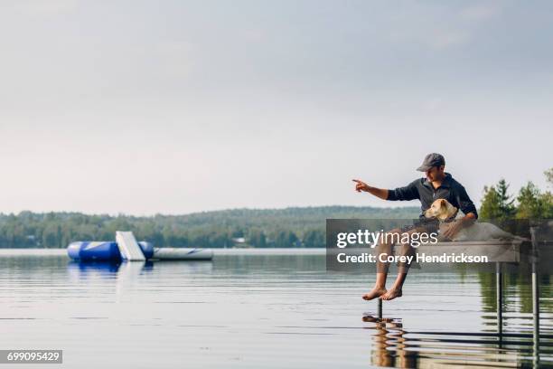 man and dog sitting on the dock at a lake. - barefoot stock pictures, royalty-free photos & images