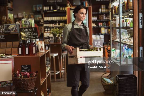 smiling owner carrying vegetable crate while walking in store - assistant imagens e fotografias de stock