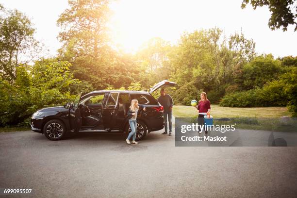 family by black electric car against trees at park - family in the park stock pictures, royalty-free photos & images