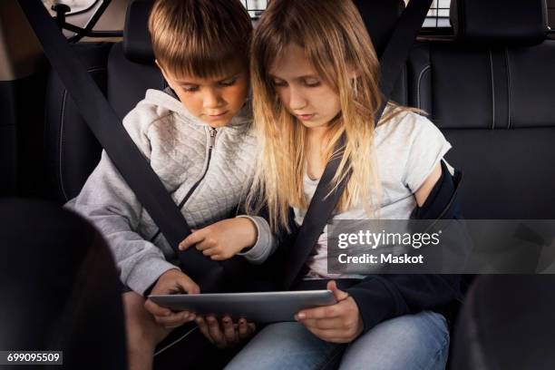 sibling using digital tablet while sitting in electric car - girl in car with ipad stock-fotos und bilder