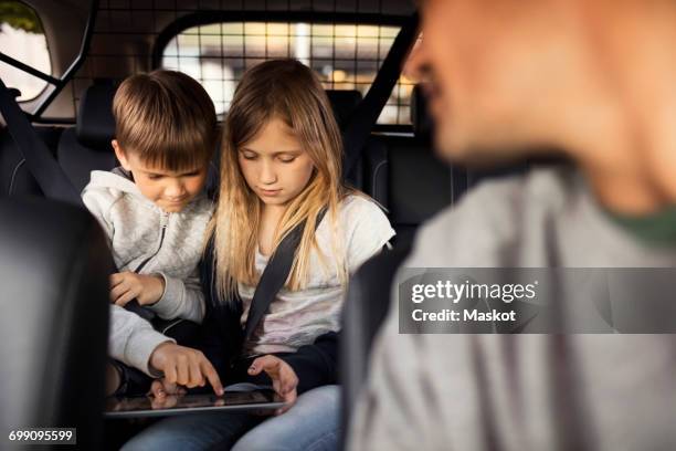 sibling using digital tablet while sitting in car with father in foreground - parental control stock pictures, royalty-free photos & images