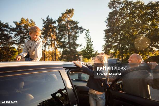 happy father and daughter looking at boy sitting on car roof - car scandinavia stock pictures, royalty-free photos & images