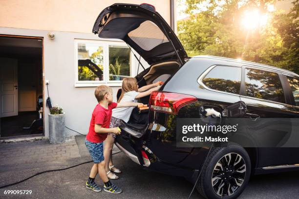kids loading black electric car trunk against house in back yard - car yard stock-fotos und bilder