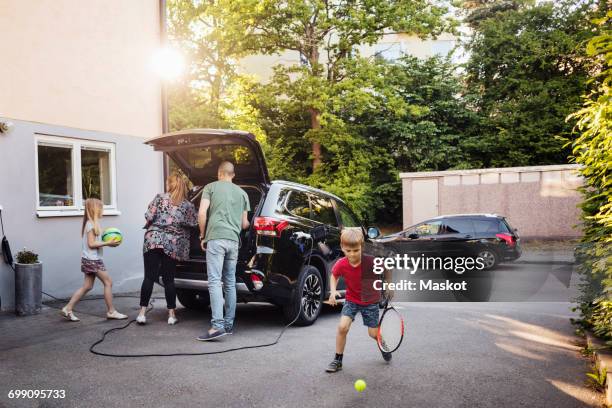 children playing with balls while parents loading car trunk in back yard - einfahrt stock-fotos und bilder