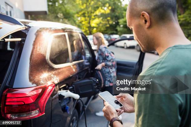 man using smartphone with woman standing by car in background - voiture digital photos et images de collection