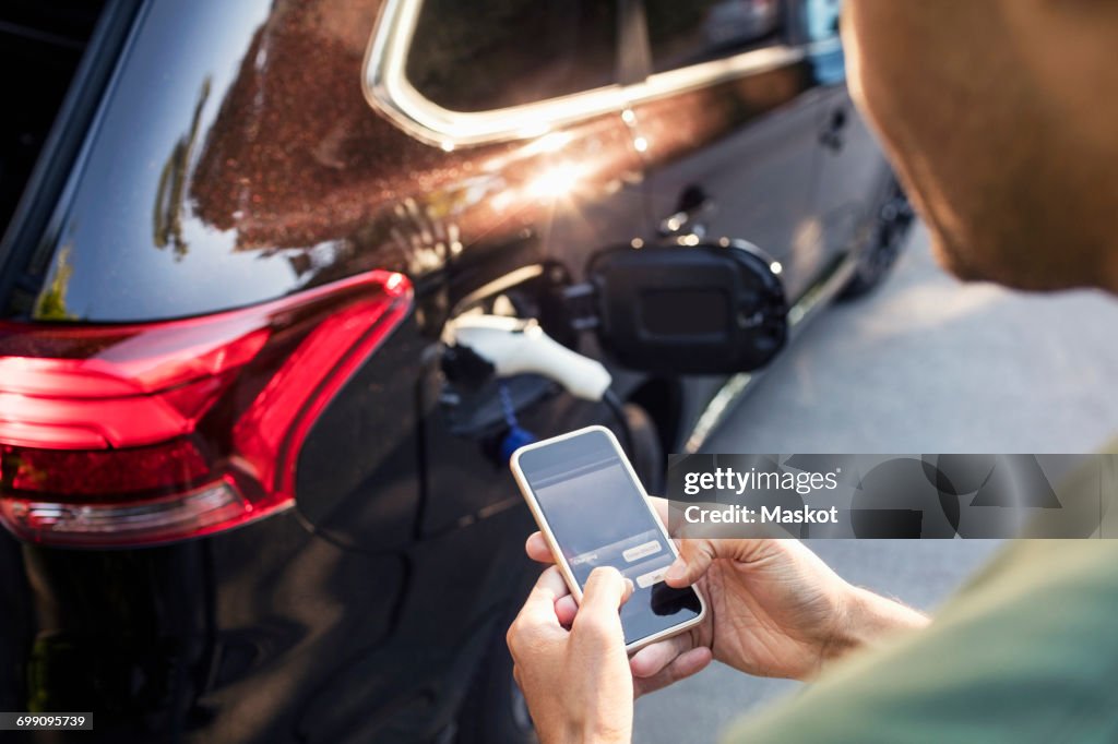 Man using mobile phone while standing by charging electric car