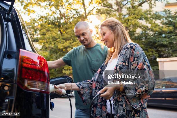 mature couple charging black electric car in back yard - red car wire 個照片及圖片檔