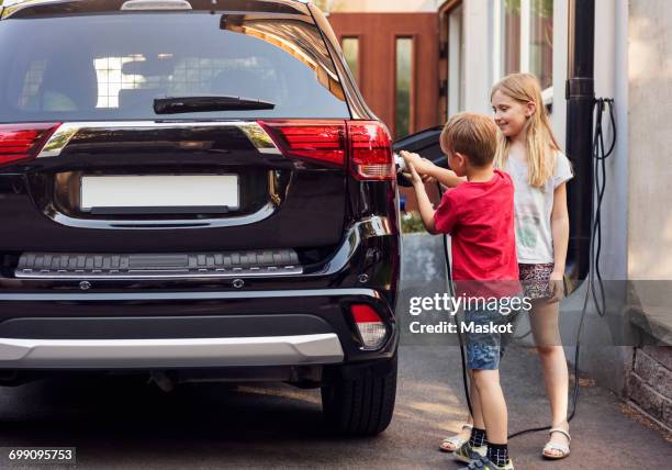 siblings charging black electric car against house - license plate stockfoto's en -beelden
