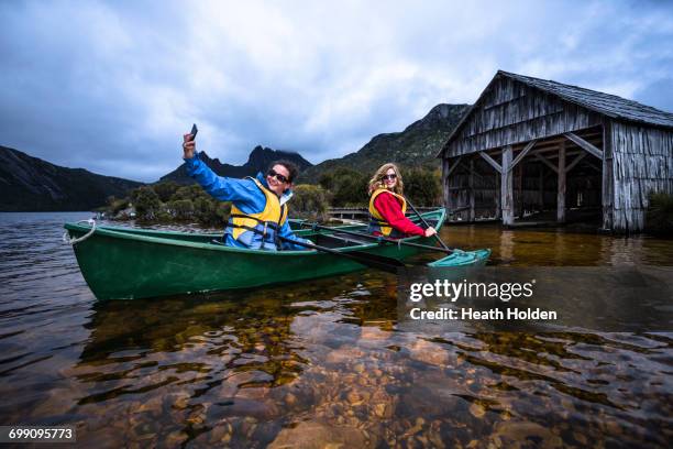 two females canoeing around the famous boat shed on dove lake at cradle mountain. - hobart stock pictures, royalty-free photos & images