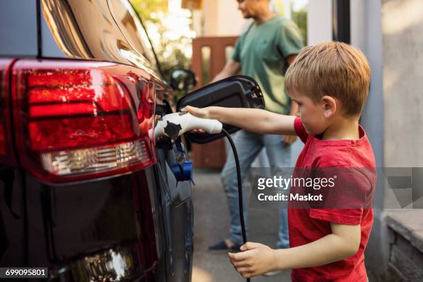 Boy charging electric car against father standing by house