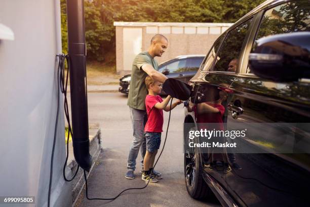 father and son charging electric car by house - electric car home stock pictures, royalty-free photos & images