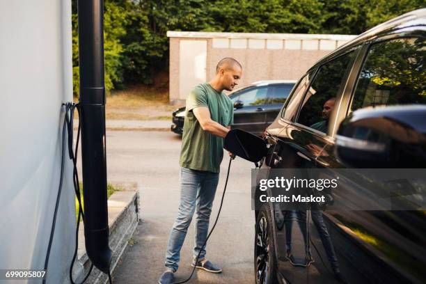 man charging electric car by house - electric car home stock pictures, royalty-free photos & images