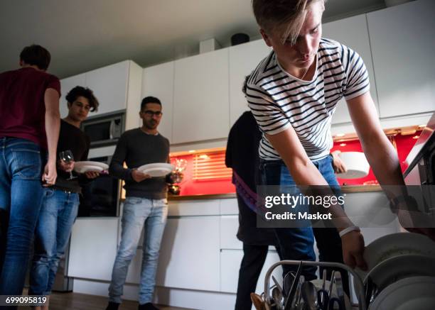 low angle view of teenage boy arranging plates in dishwasher after dinner party - reunion familia stock pictures, royalty-free photos & images