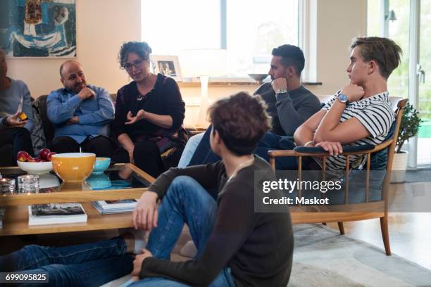 multi-ethnic friends and family talking while sitting in living room - reünie sociaal stockfoto's en -beelden