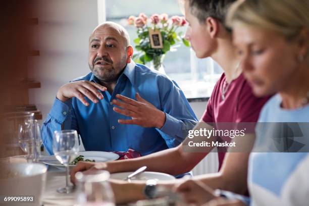 mature man gesturing while discussing with friends at dinner party - reünie sociaal stockfoto's en -beelden