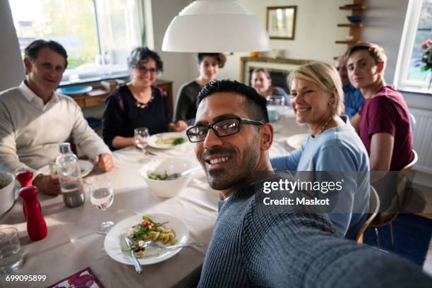 portrait of smiling man taking selfie with family and friends at dinner party - refugee portrait stock pictures, royalty-free photos & images