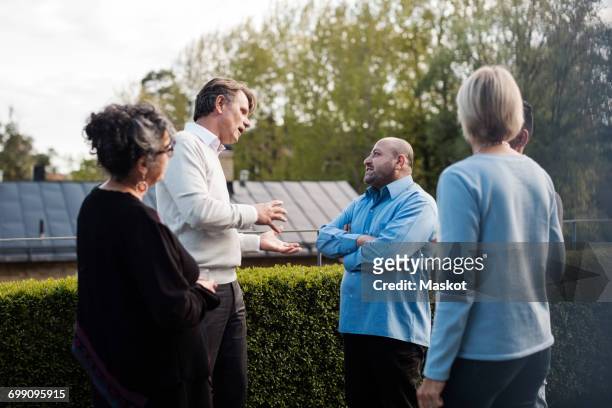 mature man gesturing while talking to friends by hedge in yard - reünie sociaal stockfoto's en -beelden