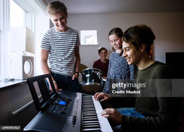 siblings looking at young man playing piano keyboard in brightly lit room - fugitivo stock-fotos und bilder