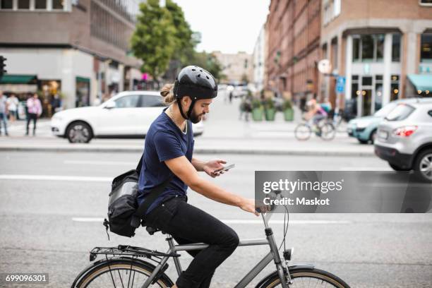 side view of man using mobile phone while riding bicycle on city street - car profile stock pictures, royalty-free photos & images