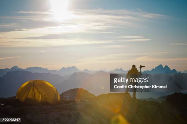 a photographer enjoys the view of the sunrise from his campsite on a rocky mountain ridge. - extreme terrain stock pictures, royalty-free photos & images