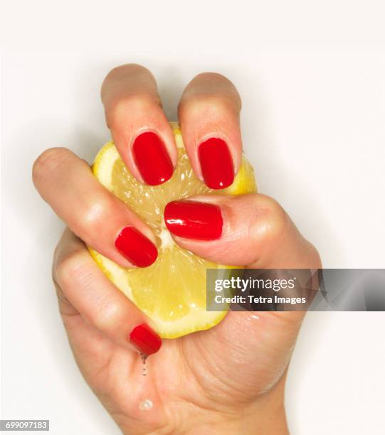 hand of woman with red nail polish squeezing lemon - quetschen stock-fotos und bilder