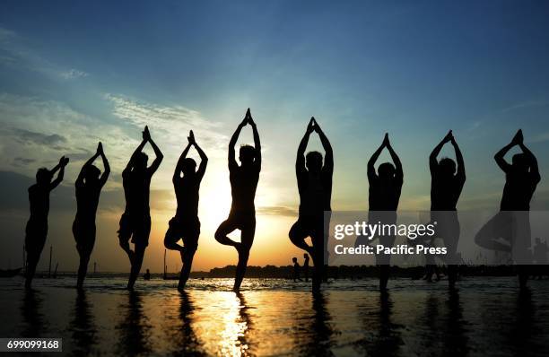 Indian youths performing yoga on the eve of International Yoga Day at Sangam River during sunset in Allahabad.
