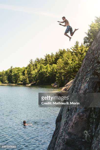 a young man is jumping off a cliff into george lake while another person is looking from under - killarney canada stockfoto's en -beelden