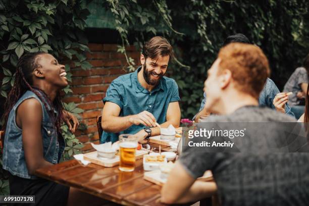 happy multi-ethnic group of people laughing at the restaurant - barbecue social gathering stock pictures, royalty-free photos & images