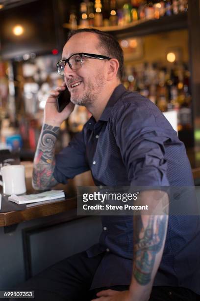barman talking on smartphone at public house counter - bar counter traditional stock-fotos und bilder