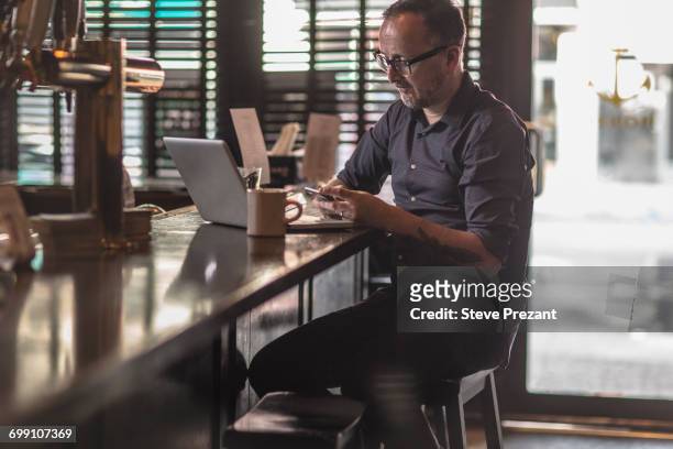 barman reading smartphone texts at public house counter - bar counter traditional stock-fotos und bilder