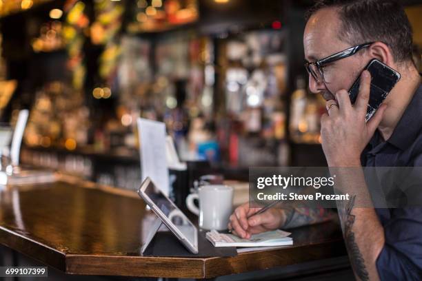 barman talking on smartphone at public house counter - bar counter traditional stock-fotos und bilder