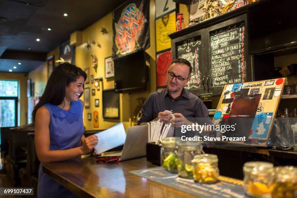barman laughing with female customer at public house counter - bar counter traditional stock-fotos und bilder