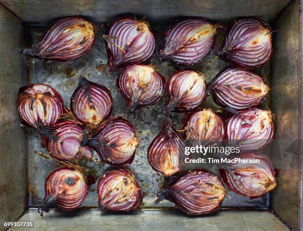 overhead view of roasted red onion halves with rosemary and olive oil in roasting tin - roasted red onion fotografías e imágenes de stock
