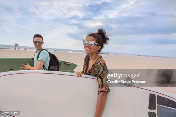 "young couple carrying surfboards on rockaway beach, new york state, usa" - rockaway beach stock pictures, royalty-free photos & images