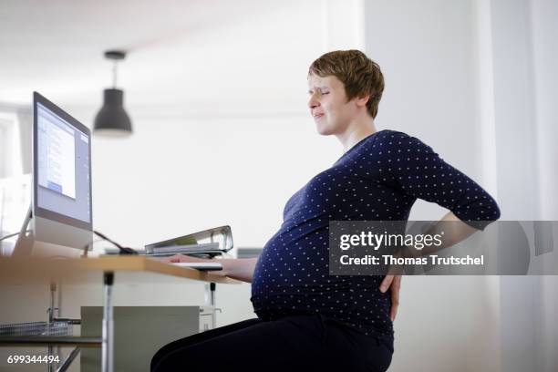 Berlin, Germany Posed scene: A pregnant woman is sitting at her desk in the office, holding her aching back on June 21, 2017 in Berlin, Germany.