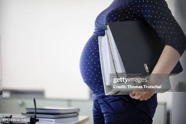 Berlin, Germany Posed scene: A pregnant woman is carrying file folders in the office on June 21, 2017 in Berlin, Germany.