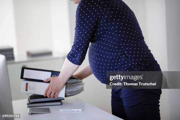 Berlin, Germany Posed scene: A pregnant woman arranges file folders on a desk in the office on June 21, 2017 in Berlin, Germany.