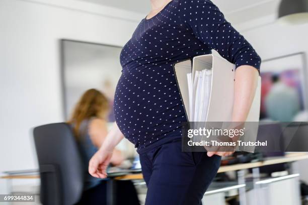 Berlin, Germany Posing scene: A pregnant woman is carrying file folders in the office on June 21, 2017 in Berlin, Germany.