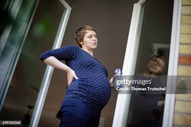 Berlin, Germany Posed scene: A pregnant woman is holding her painful back while she is cleaning windows on June 21, 2017 in Berlin, Germany.