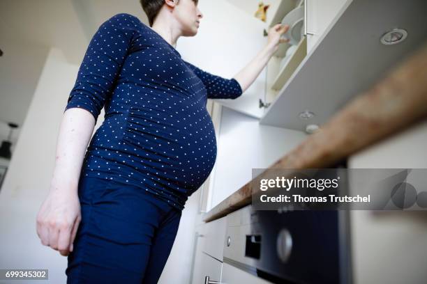 Berlin, Germany Posed scene: A pregnant woman takes a plate from a cupboard in the kitchen on June 21, 2017 in Berlin, Germany.