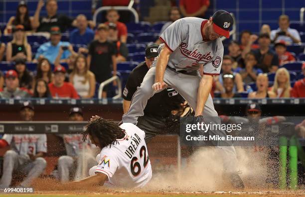 Jose Urena of the Miami Marlins scores the tying run in the eighth inning sliding under the tag from Stephen Strasburg of the Washington Nationals on...