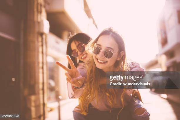 young woman on piggyback ride doing the peace sign - girlfriend stock pictures, royalty-free photos & images