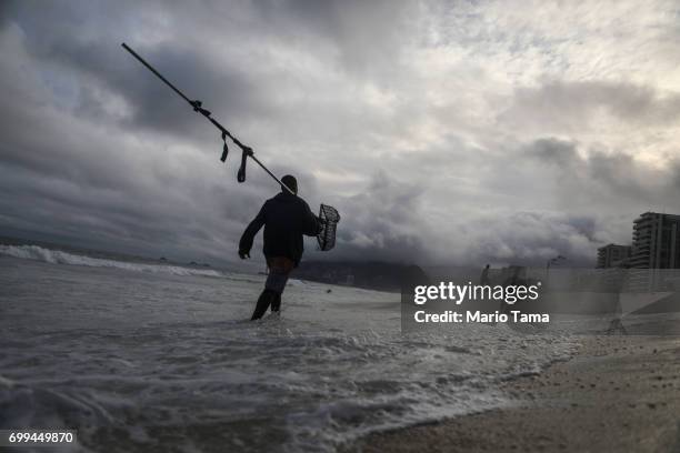 Freelance beach prospector Luis Fernando carries a sifting device which he uses to search for items lost and buried in the sand on June 21, 2017 in...
