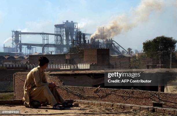This photograph taken on February 25 shows a Pakistani worker watching smoke rising from factories on the outskirts of the northwestern city of...