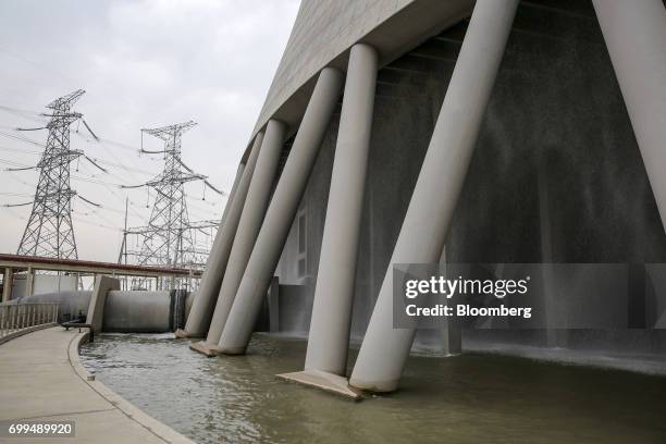 Power lines hang from transmission pylons beyond the base of a cooling tower at the Sahiwal coal power plant, owned by China's state-owned Huaneng...