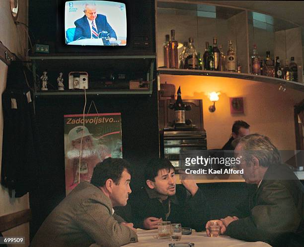 Serbian men sit in front of a television set broadcasting the second week of the war crimes trial of former Yugoslav President Slobodan Milosevic at...